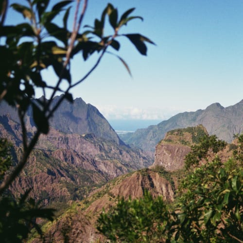 Mountainous landscape with rocky peaks and greenery in the foreground under a clear blue sky.