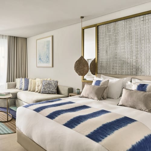 Eine luxuriöse Junior-Suite mit Meerblick im Nobu Hotel Ibiza, mit großem Bett, Dekokissen, einem Sitzbereich mit runder Teppich und Balkon mit Meerblick.