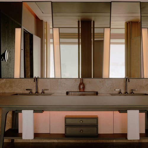 Ein modernes Hotelbadezimmer mit zwei Waschbecken, großen Spiegeln und dekorativen Vorhängen im Hintergrund.