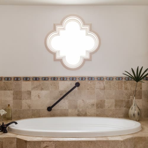Luxuriöses Badezimmer mit einer großen ovalen Badewanne, dekorativen Fliesen und einem verzierteren Fenster in einem tropischen Hotel.