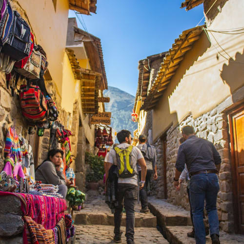 Tourists exploring a narrow street lined with colorful market stalls and traditional stone buildings.