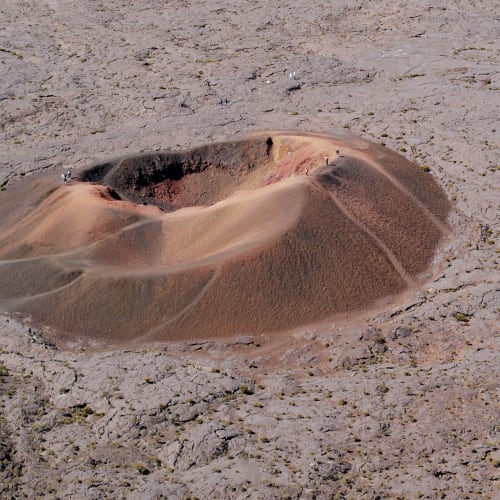 Aerial view of Piton de la Fournaise, a volcanic cone with a prominent crater surrounded by barren volcanic terrain on Réunion Island.