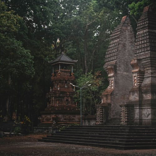 Ancient stone temple ruins surrounded by dense green trees at dusk.