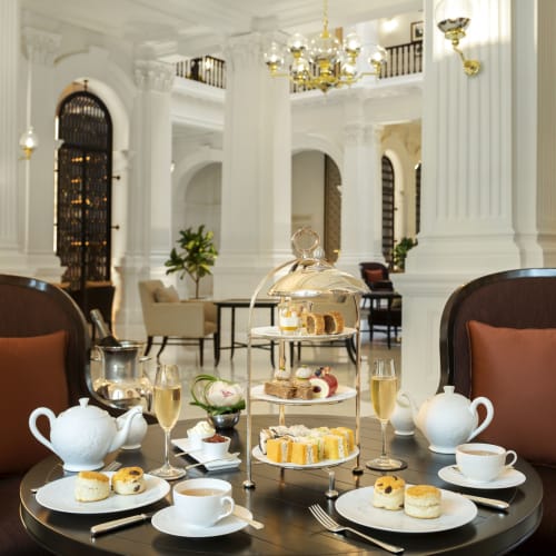Elegante Tafelgestaltung für Nachmittagstee in einer luxuriösen Hotellobby mit weißer Architektur und goldenen Akzenten.