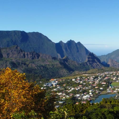 A scenic view of the town of Cilaos nestled in a valley surrounded by towering mountains under a clear blue sky.