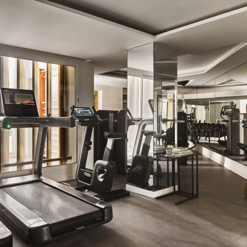 Modernes Fitnessstudio im Hotel mit Laufbändern, Trainingsfahrrädern und Spiegelwänden in einem eleganten, gut beleuchteten Raum.