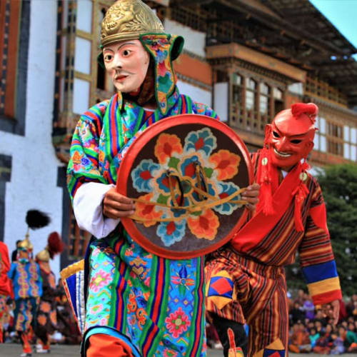 Traditionelle Maskenspieler, die während eines Festivals die bhutanische Kultur darstellen, mit Zuschauern im Hintergrund.