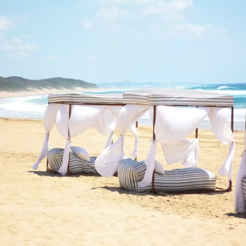 Cabanas mit weißen Vorhängen und gestreiften Kissen am Sandstrand mit Blick auf den Ozean.