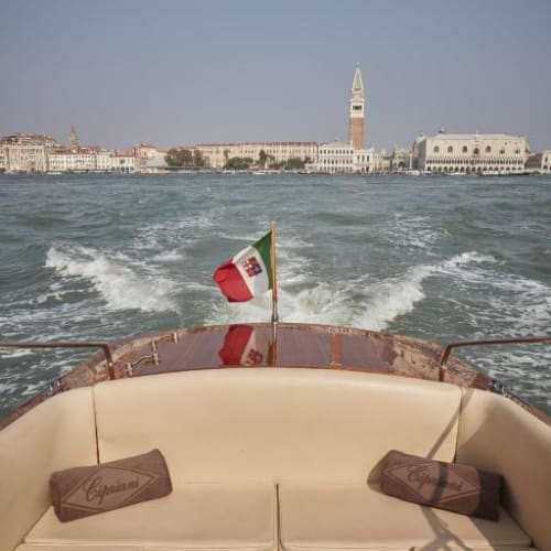A view from a boat showing a historic cityscape with a clock tower in Venice, Italy, as the boat moves through the water.