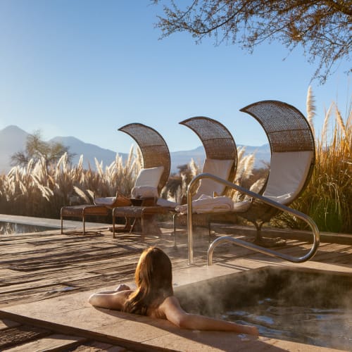 A woman relaxing in a hot tub with a scenic mountain and garden view at Tierra Atacama in Chile.