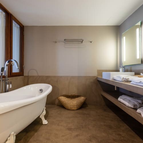 Moderne Badezimmer mit einer weißen Badewanne auf Löwenfüßen, einem großen Spiegel mit integrierter Beleuchtung und Regalen mit gefalteten Handtüchern unter der Waschtischplatte.