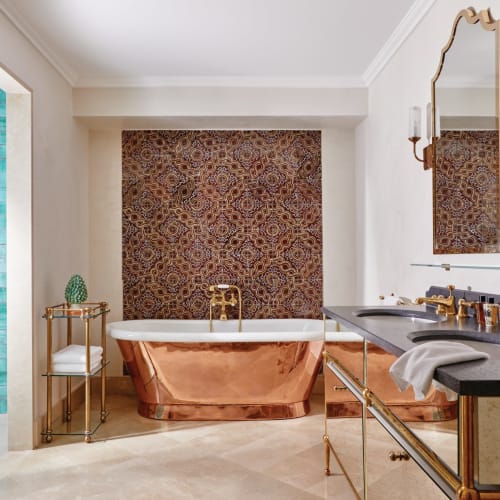 Luxurious bathroom with a copper freestanding bathtub, decorated wall, and elegant gold fixtures.