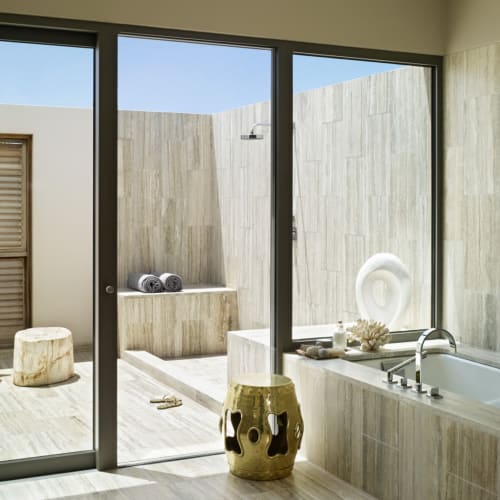 Luxurious bathroom with a bathtub, large glass doors leading outside, and minimalist decor.