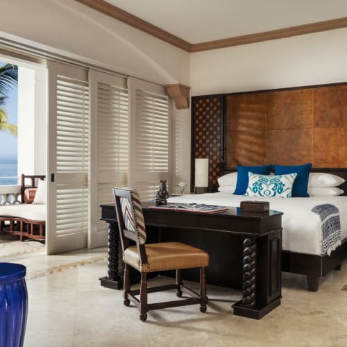 Luxuriöses Hotelzimmer mit großem Bett, Balkon mit Palmen und Meerblick sowie eleganten Einrichtungsgegenständen.