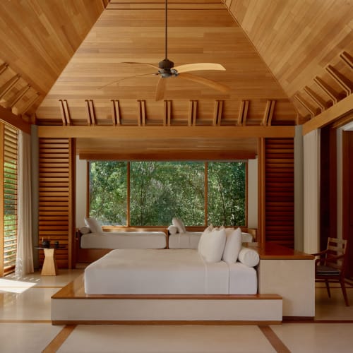 Eine luxuriöse Drei-Zimmer-Villa mit einer hohen, holzgetäfelten gewölbten Decke, großem Fenstersitz mit Blick auf die Natur und minimalistischer weißer Einrichtung.