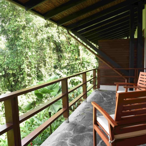 A balcony with wooden chairs and a railing overlooking lush rainforest greenery in Costa Rica.