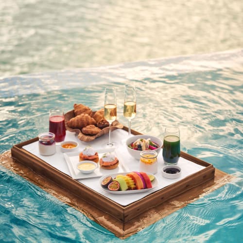 Ein schwimmendes Frühstücksservice im Pool mit Croissants, Obst, Gebäck und Getränken.