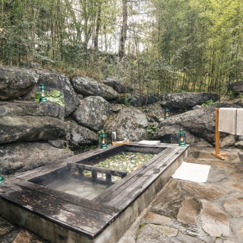 A traditional hot stone bath set in a natural outdoor setting with trees and rocks surrounding it.