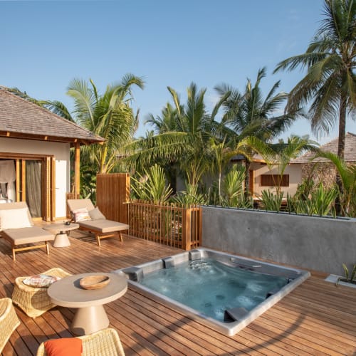 A tropical outdoor deck with a hot tub, lounge chairs, and lush palm trees in Zanzibar.