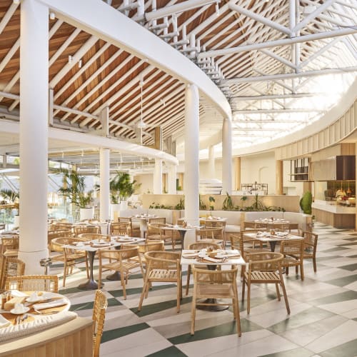 Bright and spacious restaurant with modern decor, round tables set for dining, and large windows letting in natural light.