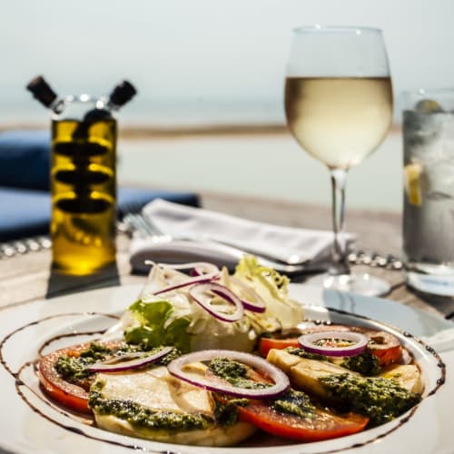Ein Meeresfrüchtesalat mit Tomaten, Mozzarella und Kräutern auf einem weißen Teller, im Sonnenlicht an einem Unterhaltungsplatz am Strand serviert.