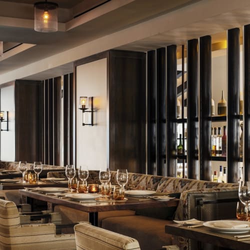 Elegantes Restaurantinterior mit moderner Beleuchtung, Holzakzenten und schön gedeckten Tischen mit Gläsern und Kerzen.