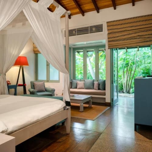 Ein Schlafzimmer mit einem Himmelbett, einem Sofa mit Kissen, einem Fenster mit Blick auf einen Garten und modernen Möbeln.