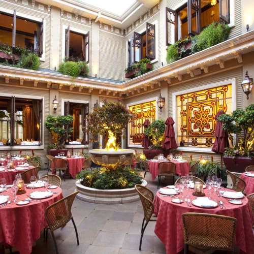 Eleganter Außenhof mit Tischen mit roten Tüchern, Topfpflanzen und dekorativen Wandpanelen.