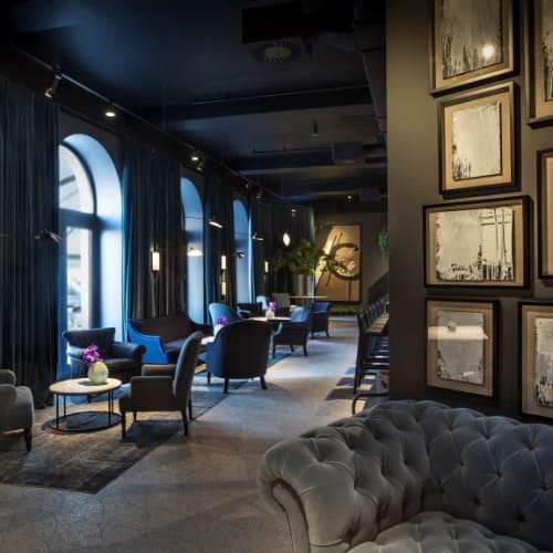 A cozy hotel lounge with dark walls, arched windows, and comfortable chairs arranged for guests, with framed artwork on the wall.