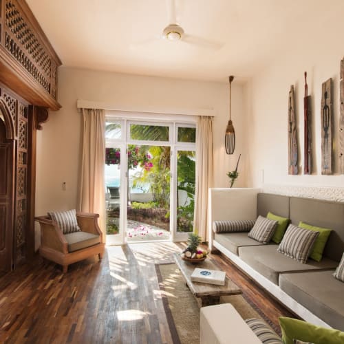 Bright living room with wooden flooring, large window with curtains, and a garden view, decorated with modern furniture and wall art.