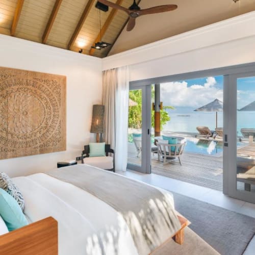 Luxus-Villa-Schlafzimmer mit großem Bett, moderner Dekoration und einer Schiebetür, die zu einer Terrasse mit Outdoor-Möbeln und Blick auf den Ozean und die Inseln führt.