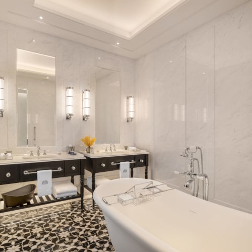 Luxuriöses Badezimmer mit einer weißen Badewanne, Doppelwaschbecken und eleganten Lichtleuchten in einem Marmorraum.