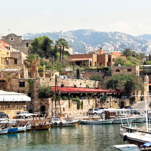 Die historische Hafenstadt Byblos mit Booten im Hafen, steinernen Gebäuden und einer hügeligen Umgebung.
