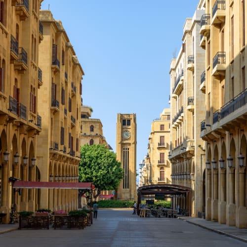 Leere Straße im Stadtzentrum von Beirut mit Cafés und hohen historischen Gebäuden unter klarem blauen Himmel.