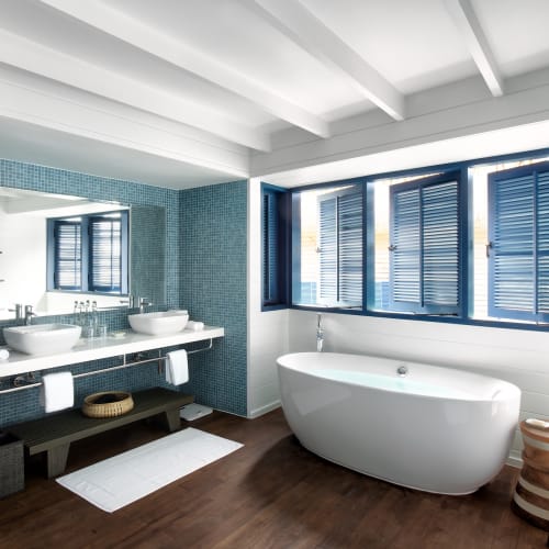 Luxurious bathroom with a standalone bathtub, blue window shutters, and a double sink in a beachside villa.