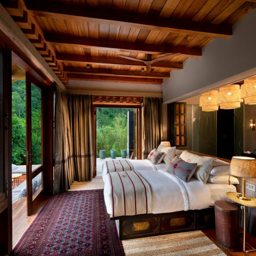 Eine luxuriöse Familiensuite mit zwei Betten in einer gemütlichen Berghütte, mit Holzbalken an der Decke, großen Fenstern und eleganter Dekoration mit Lampen und Vorhängen.