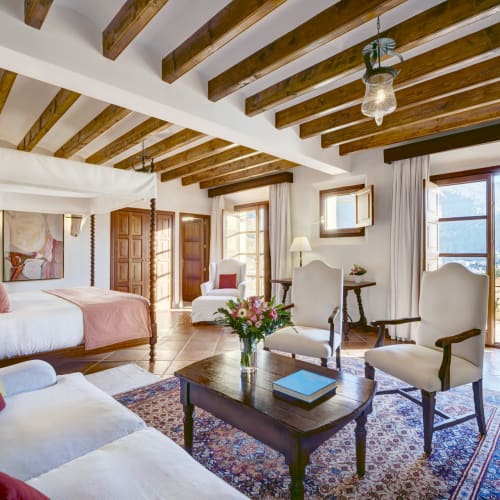 Luxuriöses Schlafzimmer mit Holzdeckenbalken, großen Fenstern mit Blick und eleganter Einrichtung.