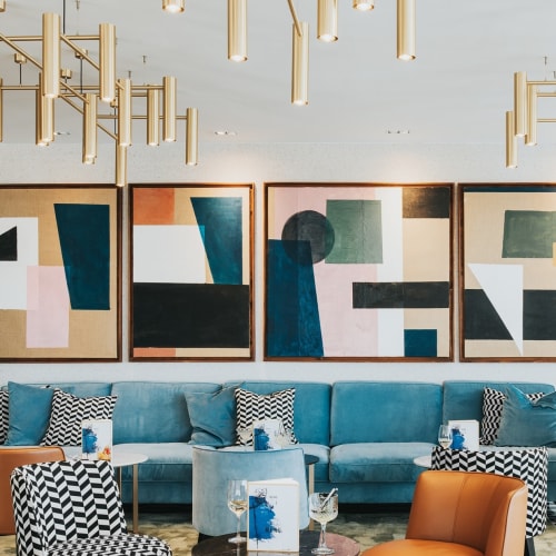Modernes Hotelrestaurant mit abstrakter Kunst, blauer Couch, gemusterten Stühlen und goldenen Leuchterketten.