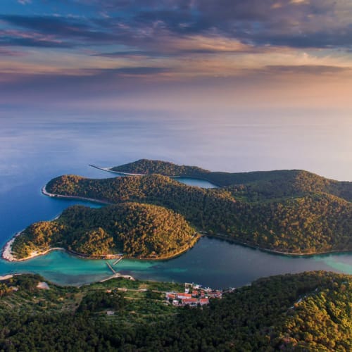 Aerial view of the scenic island of Mljet in Croatia with lush green forests and a calm blue sea under a colorful sky.