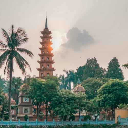 A pagoda with a tall, multi-tiered spire surrounded by lush greenery and palm trees.