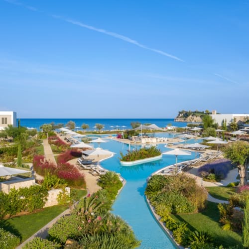 Ein malerischer Blick auf das Sani Dunes Resort mit üppigen Gärten, einem gewundenen blauen Pool und modernen Gebäuden mit Blick auf das Meer.
