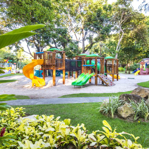 Bunter Holzspielplatz mit Rutschen und Kletterstrukturen in einer üppigen, grünen Parklandschaft.