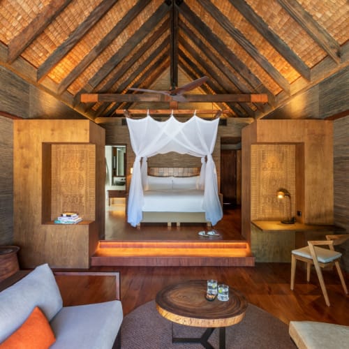Luxurious bedroom with a canopy bed in a tropical resort suite featuring wooden accents and cozy seating area.
