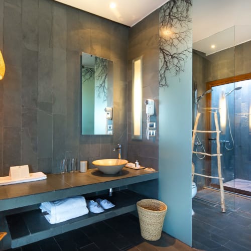 Modern bathroom with dark tiled walls, a basin sink, and an open shower area with a wooden framework.