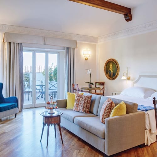 Luxus-Suite mit großem Bett, Sofa und Balkonblick in einem hellen, elegant dekorierten Raum.