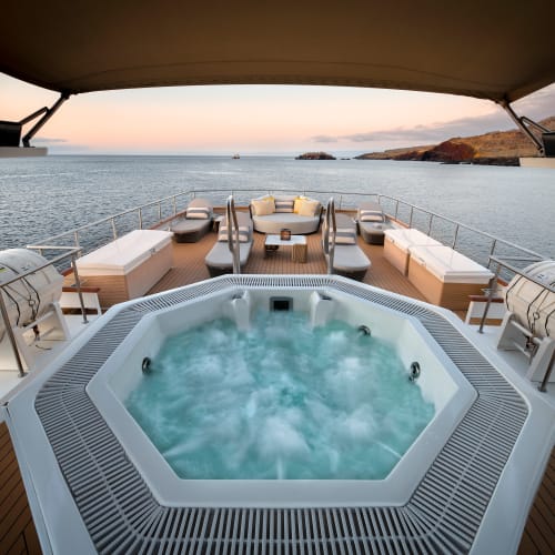 Ein Whirlpool mit sprudelndem Wasser auf dem Deck eines Luxusyacht, blickend auf das Meer und entfernte Inseln.