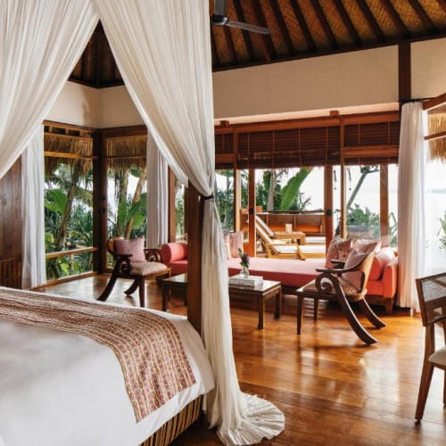 Luxuriöses Schlafzimmer mit einer vierpfostenbett, Sitzecke und großen Fenstern mit Blick auf tropisches Grün.