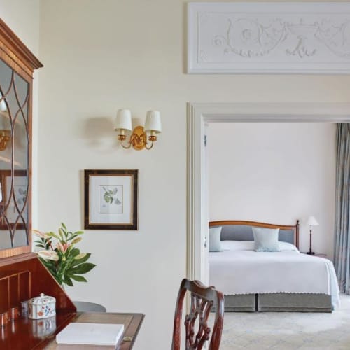 Ein luxuriöses Hotelzimmer mit einem Wohnbereich, sichtbar von einem angrenzenden Raum, mit eleganten Möbeln und Dekoration.