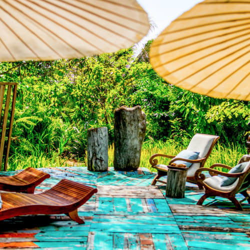 A serene outdoor lounge area on a private island with wooden furniture, large umbrellas, and lush greenery in the background.