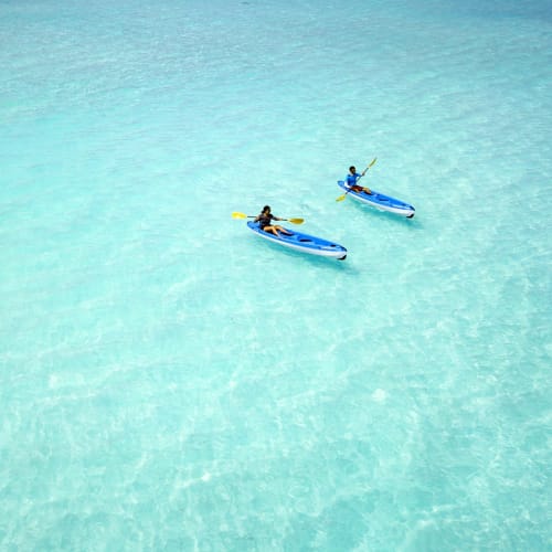 Two people are kayaking in clear, turquoise water on Milaidhoo Island, Maldives.